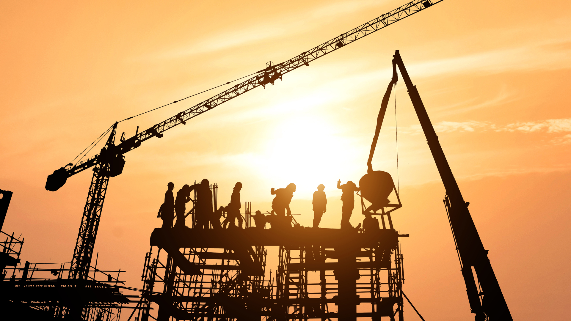 Workers on skyscraper being built with sun setting in background.